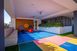A modern interior with a geometric wall design, a ceiling fan, and a colorful play area. - Soho Skies 204 Stunning Sunset - Ocean Views wit (Puerto Vallarta)