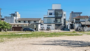 A modern building with multiple floors, a parking area with cars, and a clear sky. - Oceanfront Studio Campeche Beach Aar0203 (Florianópolis)