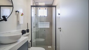 A modern bathroom with a glass-enclosed shower, a white sink, and a mirror above it. - Oceanfront Studio Campeche Beach Aar0203 (Florianópolis)