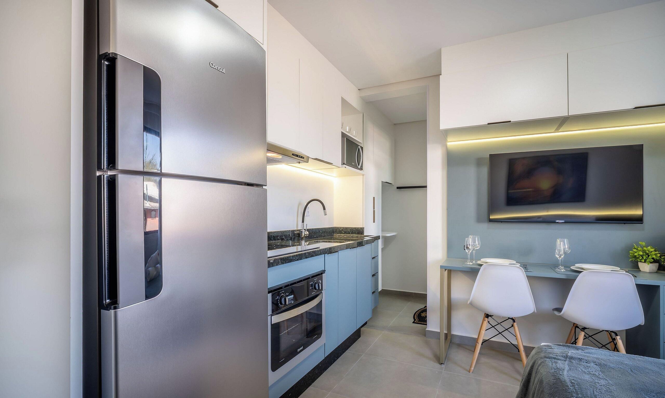 A modern kitchen with stainless steel appliances, a built-in oven, and a dining area with a TV above the counter.