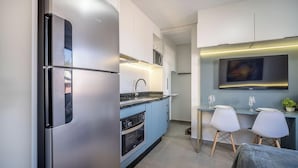 A modern kitchen with stainless steel appliances, a built-in oven, and a dining area with a TV above the counter. - Oceanfront Studio Campeche Beach Aar0203 (Florianópolis)