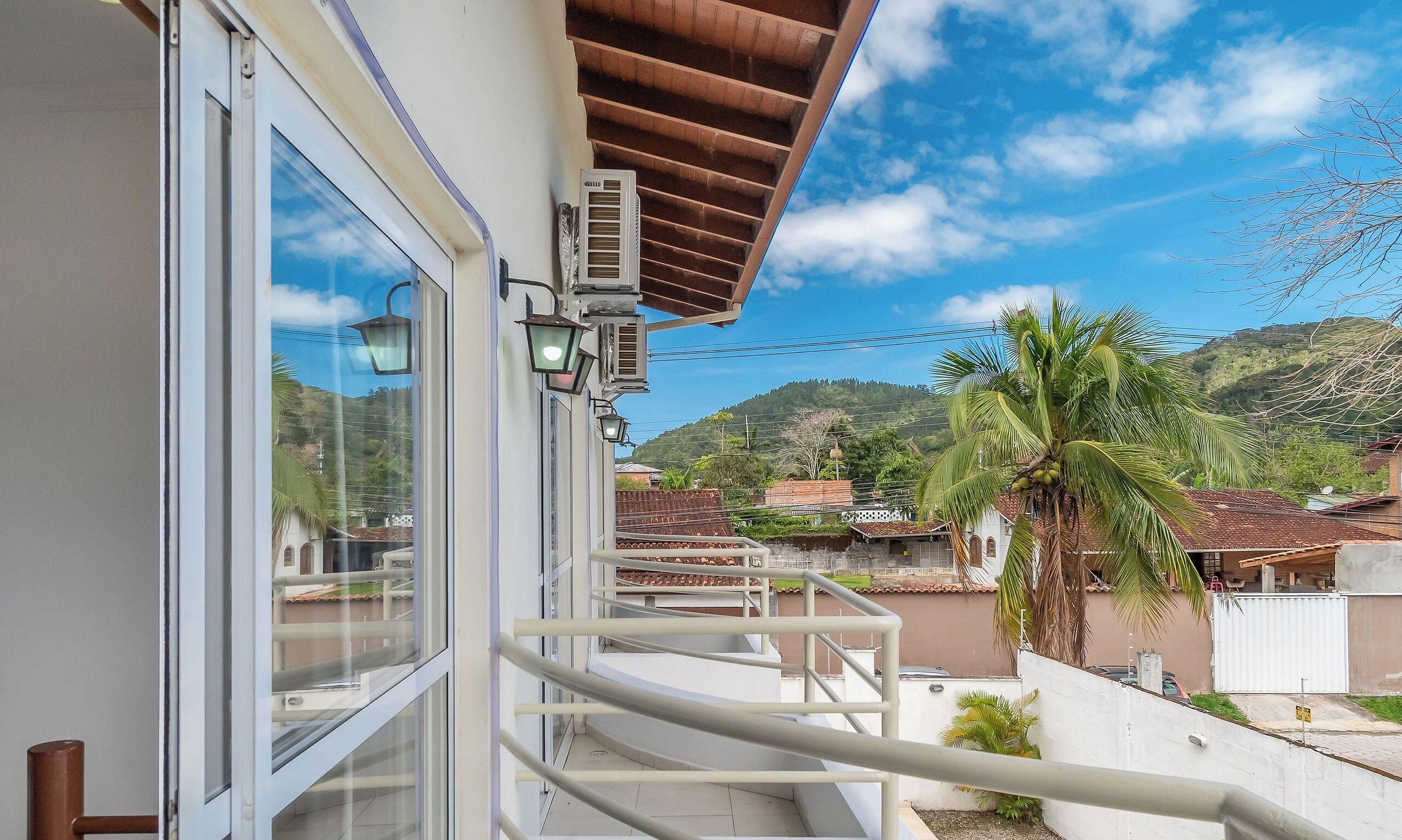 Un balcón con vistas a una zona residencial, una palmera y una montaña al fondo.