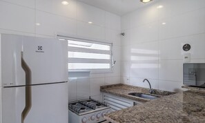 A modern kitchen with white cabinetry, a built-in gas stove, a stainless steel sink, and a refrigerator. - Apt w/ Balcony 350m From the Sea, Ubatuba Fua0004 (Ubatuba)