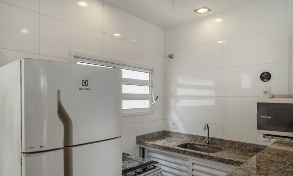A modern kitchen with a stainless steel refrigerator, a granite countertop, a built-in oven, and a wall-mounted television. - Apt With Balcony 350 m From the Beach Fua0002 (Ubatuba)