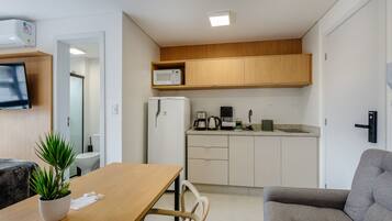 A compact kitchen with a microwave, coffee maker, and refrigerator. There is a dining table with chairs and a potted plant.