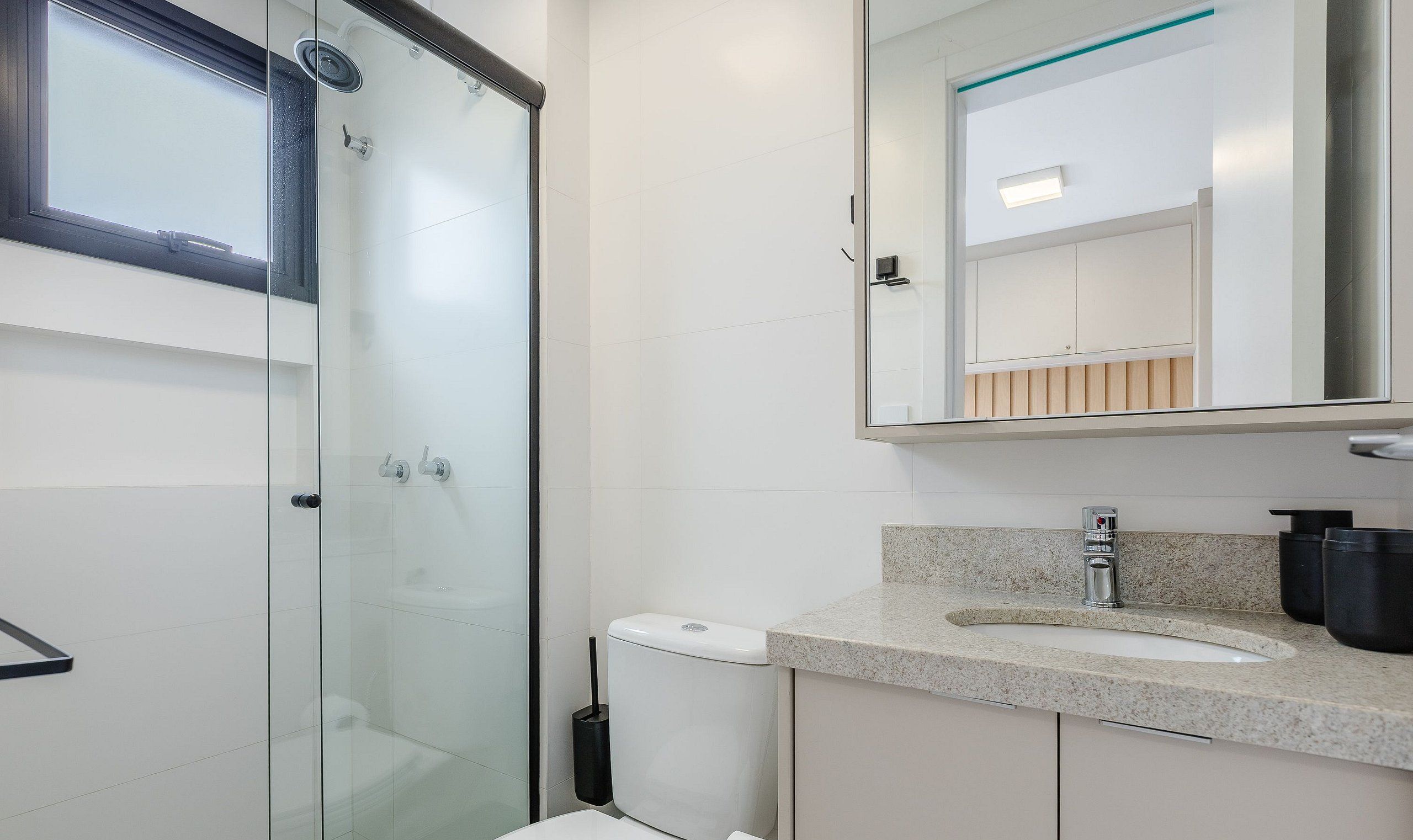 A modern bathroom with a glass shower enclosure, a white toilet, and a granite countertop with a sink and mirror.