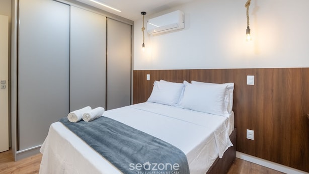 A bedroom with a bed, a wooden headboard, an air conditioning unit, and a wall-mounted light fixture. - Apt in Guarapari Center, 300m From the Sea Eep0602 (Guarapari)