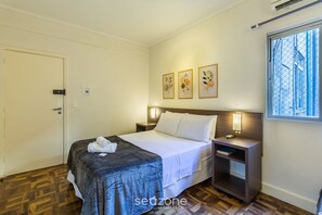 A hotel room with a bed, bedside table, and a window with a view of the outside. - Studio in the Historic Center of PoA Els0902 (Porto Alegre)