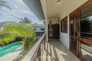 Un balcón con vistas a una piscina, una puerta de madera y suelo de baldosas.