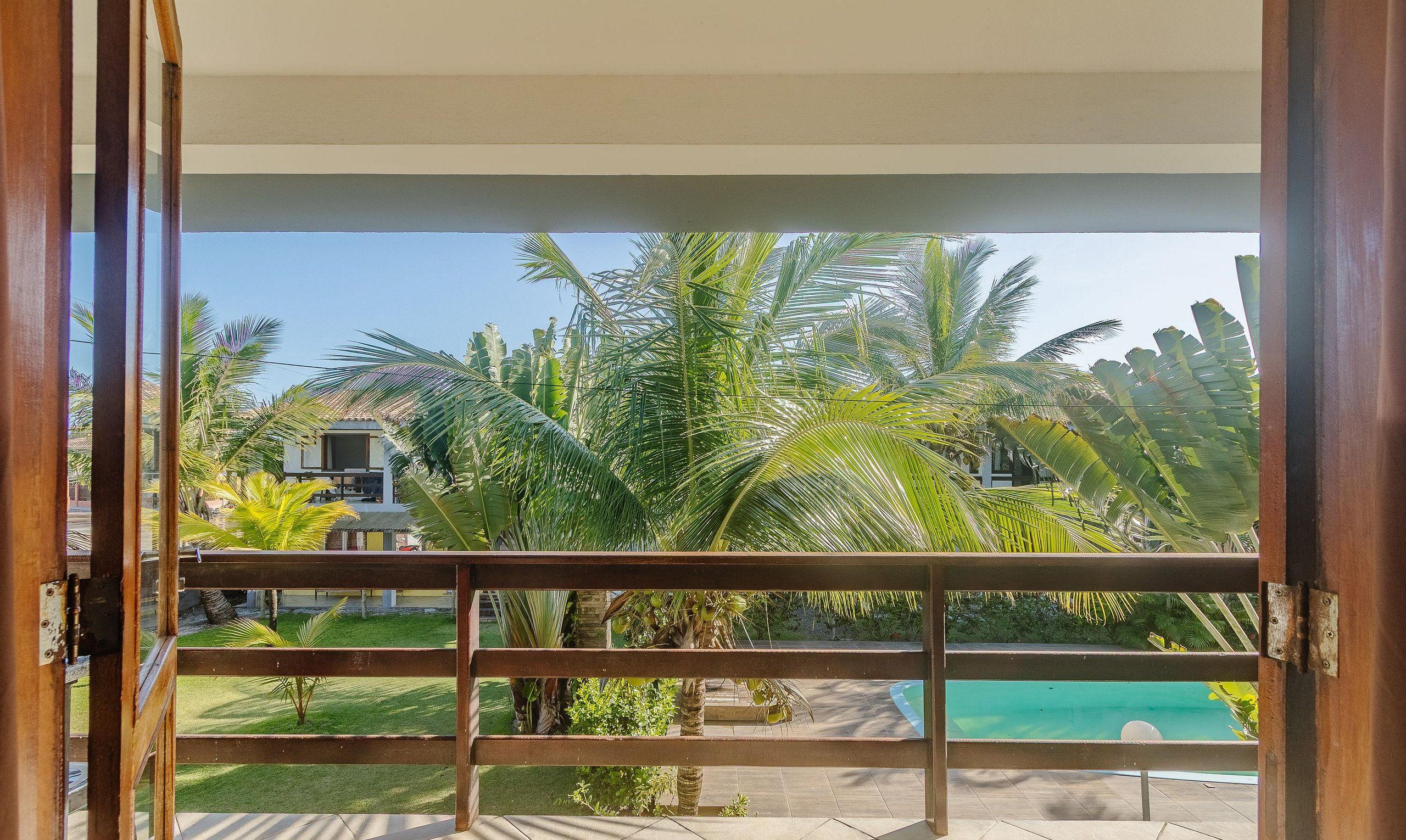 Vista desde un balcón con piscina, palmeras y un edificio al fondo.