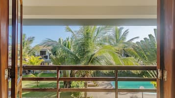 Vista desde un balcón con piscina, palmeras y un edificio al fondo.
