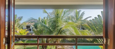 A view from a balcony with a pool, palm trees, and a building in the background.