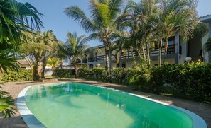 Piscina cercada por palmeiras e um edifício com varandas.