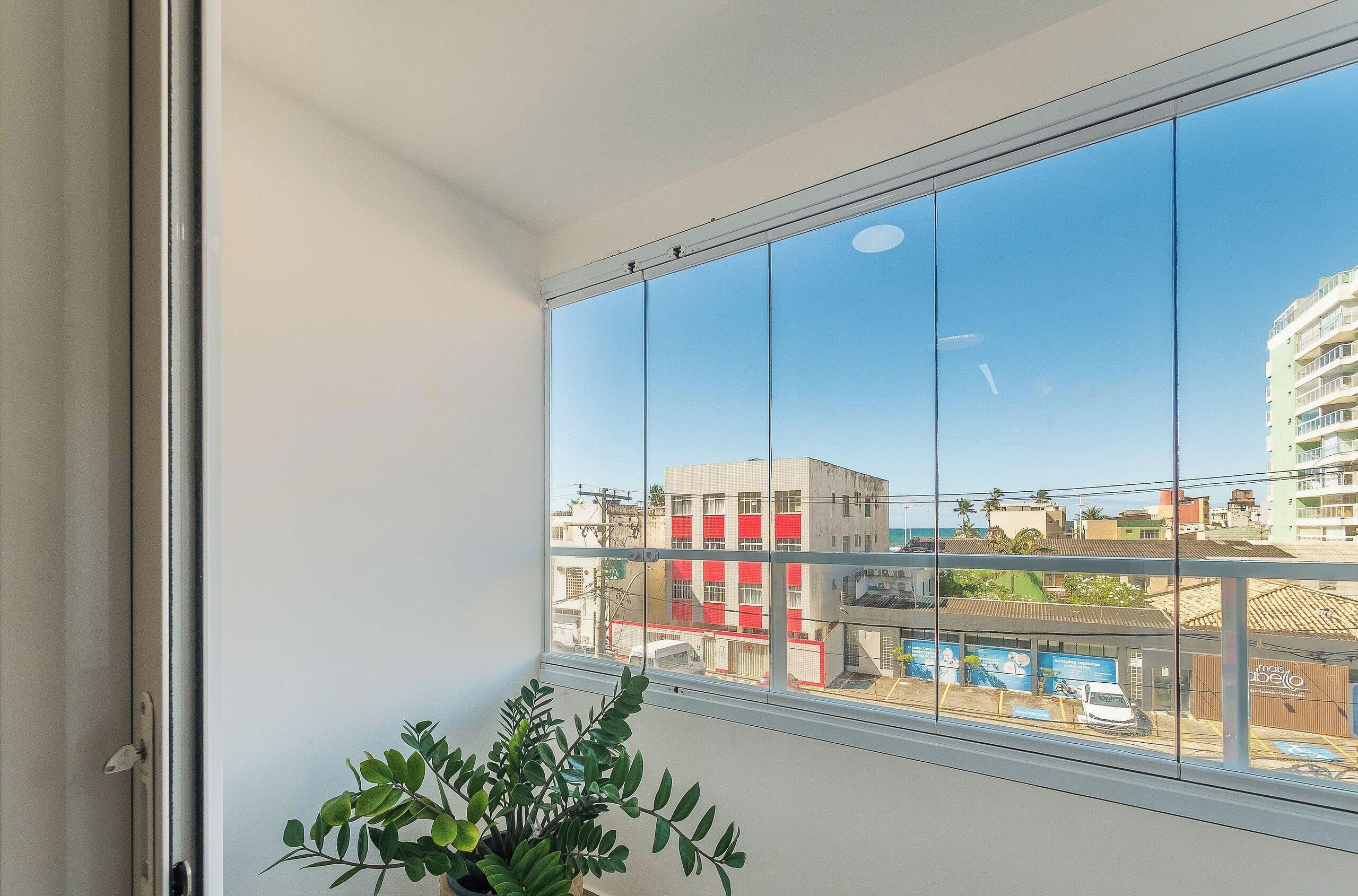 A room with a large window offering a view of a cityscape, a potted plant, and a door.