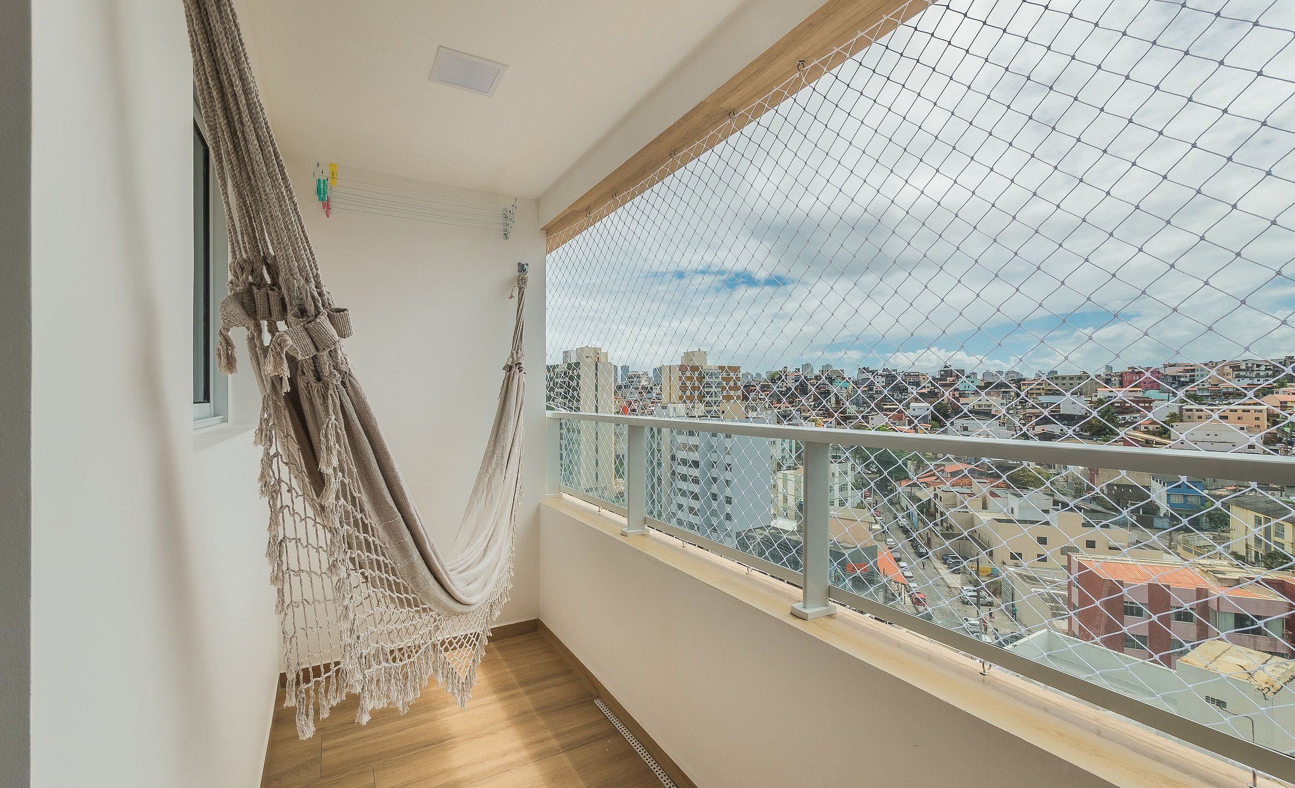 A balcony with a macrame hammock, a view of a cityscape, and a metal railing.