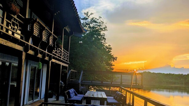 Um deck de madeira com área de estar externa e vista para um pôr do sol sobre a água.