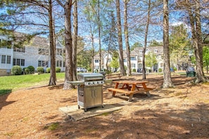 A picnic area with a grill and benches, surrounded by trees and residential buildings.