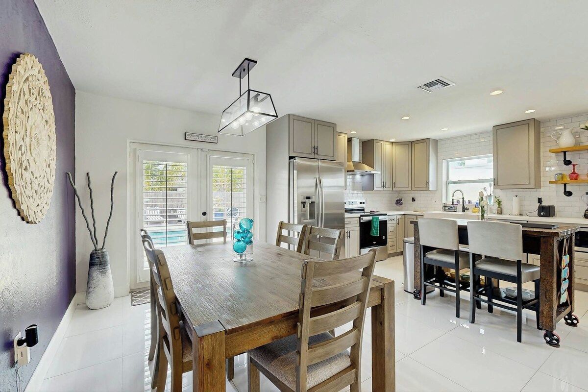 Una cocina moderna con una isla central, electrodomésticos de acero inoxidable y un comedor con sillas de madera.