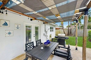 Een overdekt terras met een tafel, stoelen, een barbecue en een hek op de achtergrond.