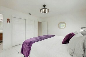 Een slaapkamer met een bed, een plafondventilator, een deur en een spiegel aan de muur.
