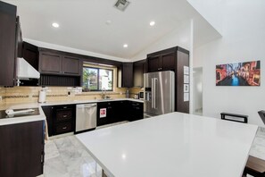 A modern kitchen with dark cabinetry, a stainless steel refrigerator, and a large island. - Marble House in Lauderdale Harbours (Fort Lauderdale)