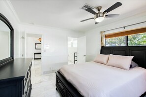 A bedroom with a bed, a ceiling fan, a window with curtains, and a door leading to another room. - Marble House in Lauderdale Harbours (Fort Lauderdale)