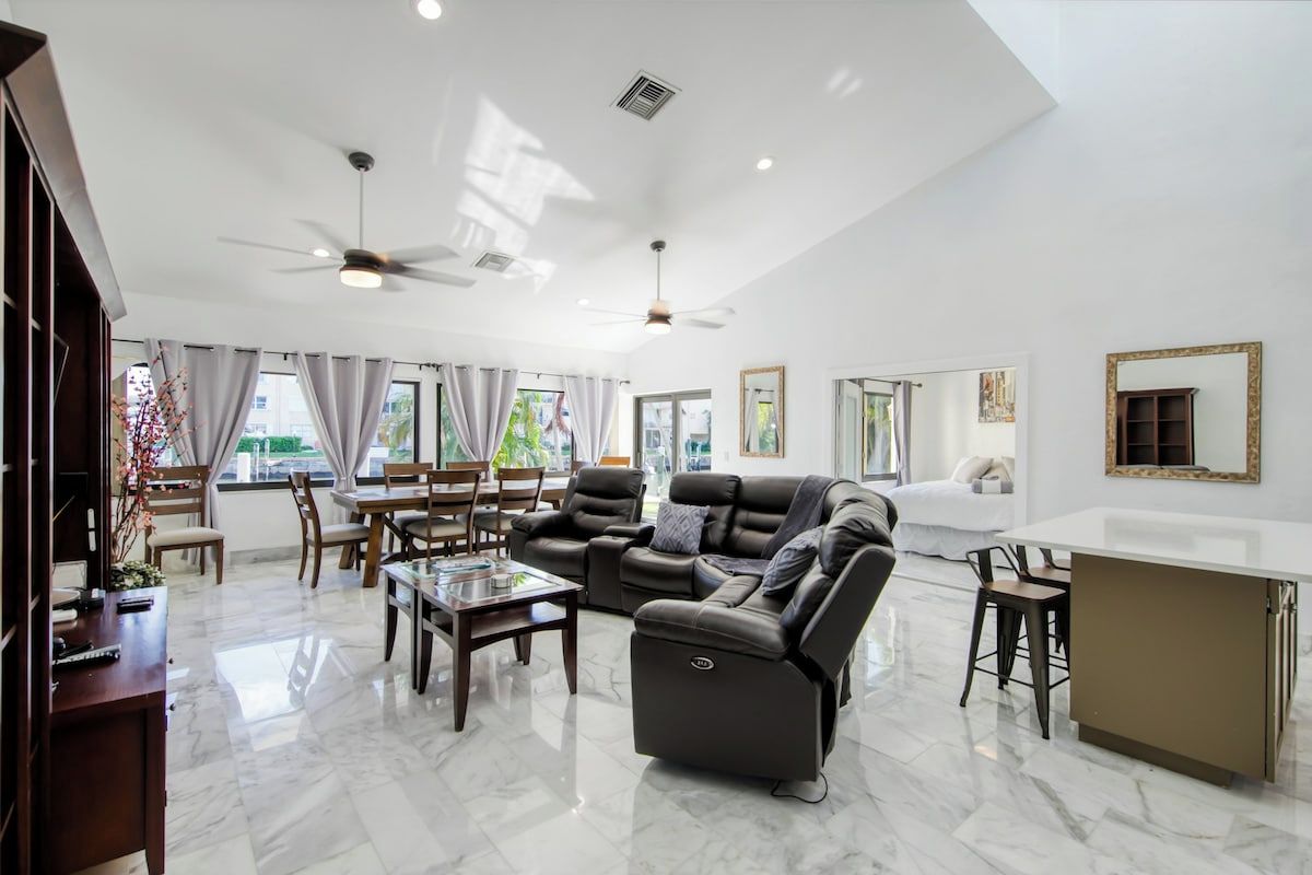 A spacious living room with a modern design, featuring a large sofa, a dining area, and a kitchen area.