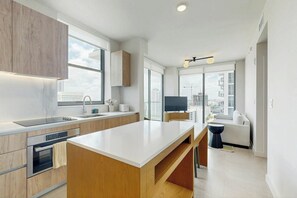 A modern kitchen with a central island, built-in oven, and a large window offering a city view. - Luxe in the Sky - Skyline Views (Miami)