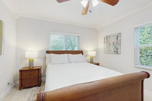 A bedroom with a bed, two bedside tables, a ceiling fan, and a window with blinds. - The Front House & Cottage (Fort Lauderdale)