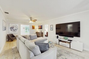 A modern living room with a sectional sofa, a flat-screen TV, and artwork on the walls. - The Front House & Cottage (Fort Lauderdale)