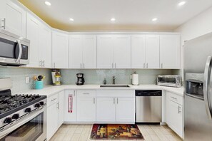 A modern kitchen with white cabinets, a microwave, a stove, a dishwasher, and a refrigerator. - The Front House & Cottage (Fort Lauderdale)