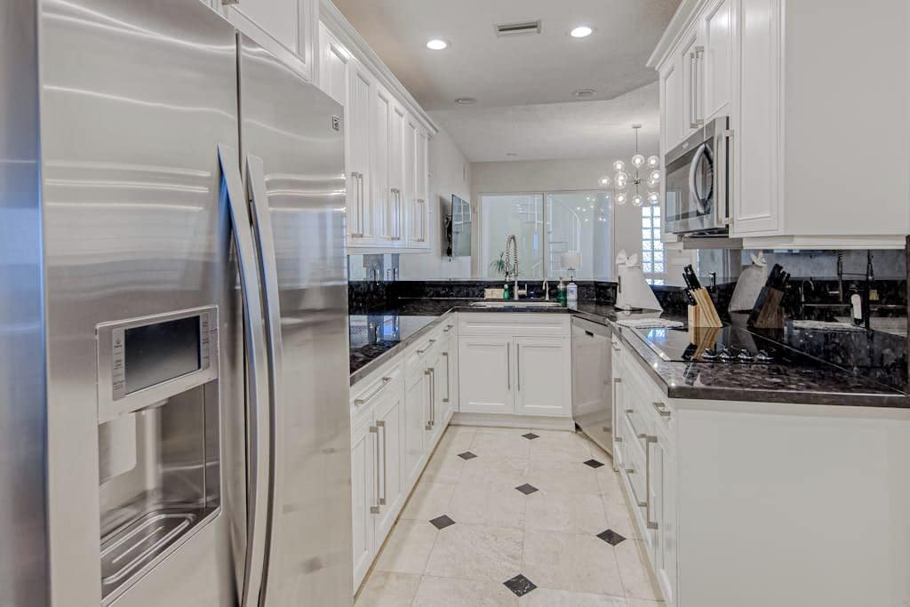 A modern kitchen with white cabinetry, a stainless steel refrigerator, and a black marble countertop.
