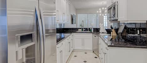 A modern kitchen with white cabinetry, a stainless steel refrigerator, and a black marble countertop.