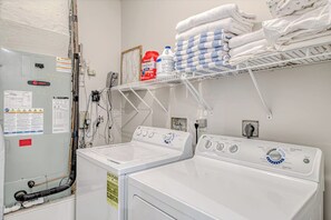 Un espace buanderie comprenant deux machines à laver, une étagère avec des serviettes pliées et une bouteille de lessive.