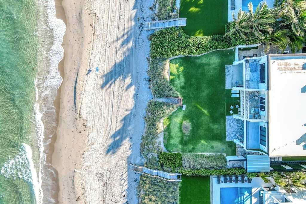 Vista aérea de una propiedad frente a la playa con piscina, un área de patio y un puente que conecta con la playa.