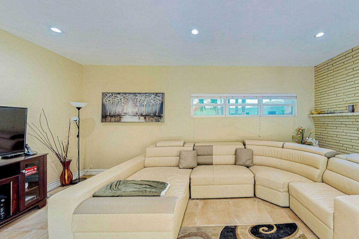 A living room with a sectional sofa, a flat-screen TV, a vase, and a painting on the wall.