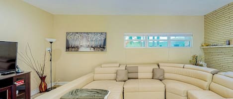 A living room with a sectional sofa, a flat-screen TV, a vase, and a painting on the wall.