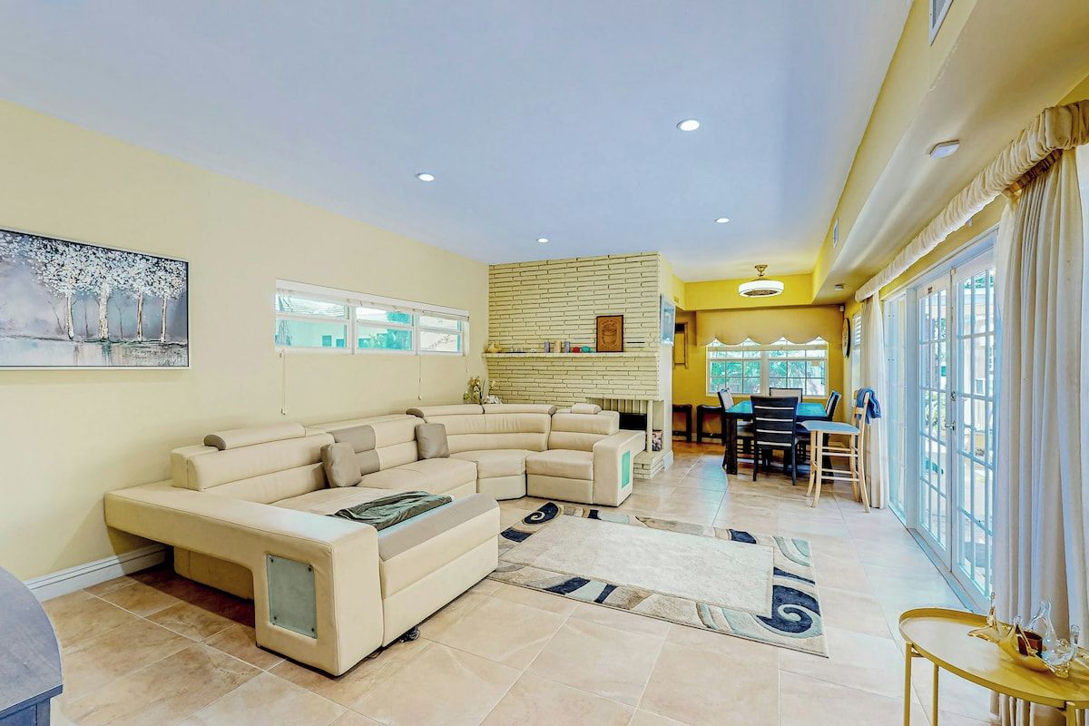 A spacious living room with a sectional sofa, a dining area with a table and chairs, and large windows allowing natural light.