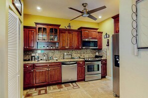 A kitchen with wooden cabinets, stainless steel appliances, a ceiling fan, and a patterned floor. - Go with the Flow - Pet Friendly (Hollywood)