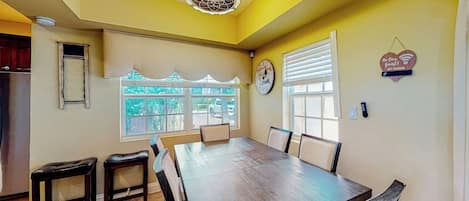 A dining area with a large table and chairs, a ceiling fan, and a window with blinds.