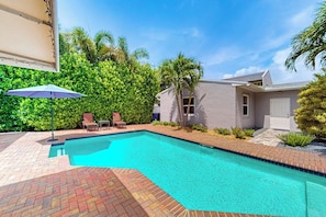 A swimming pool with a brick border, surrounded by a patio area with chairs and an umbrella. - The Cottage - Private Pool (Fort Lauderdale)