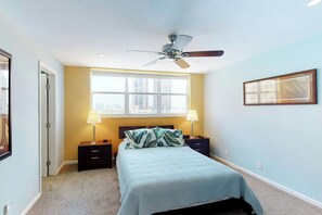 Ein Schlafzimmer mit einem Bett, zwei Nachttischen, einem Deckenventilator, einem Fenster mit Blick und einem gerahmten Bild an der Wand.