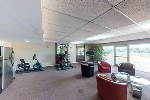 Ein Fitnessraum mit Trainingsgeräten, eine Sitzecke mit Stühlen und große Fenster.