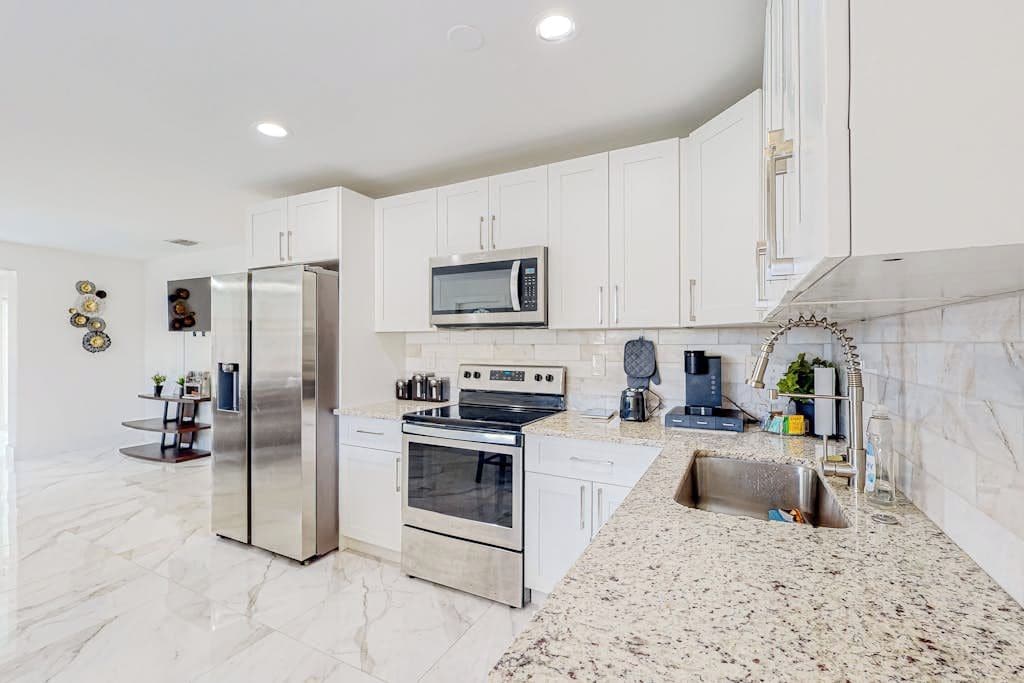 A modern kitchen with white cabinetry, stainless steel appliances, and a granite countertop.