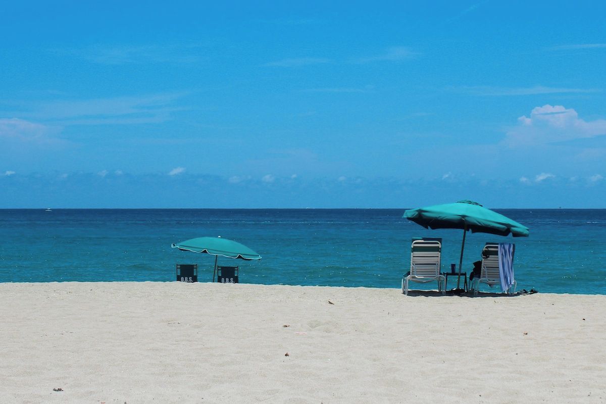 Una platja amb dues ombrel·les i cadiretes, un cel serè i l'oceà al fons.