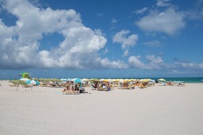 Ein Strand mit vielen Sonnenschirmen und Liegestühlen, einem Rettungsturm und blauem Himmel.