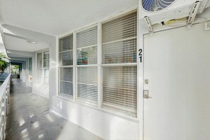 A corridor with a series of windows, a door with a number, and a ceiling fan. - Sunshine, Beach & Smiles on Ocean Drive (Miami Beach)
