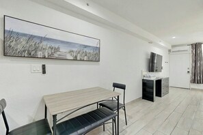 A modern room with a dining table, chairs, a bench, a flat-screen TV, a built-in oven, and a large painting on the wall. - Sunshine, Beach & Smiles on Ocean Drive (Miami Beach)