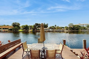 A wooden deck with a table and chairs overlooking a calm body of water, with buildings and trees in the background. - Middle River Lookout (Fort Lauderdale)
