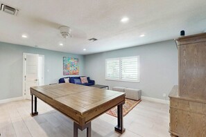 A spacious room with a wooden dining table, a ceiling fan, a sofa with cushions, and a window with blinds. - Middle River Lookout (Fort Lauderdale)